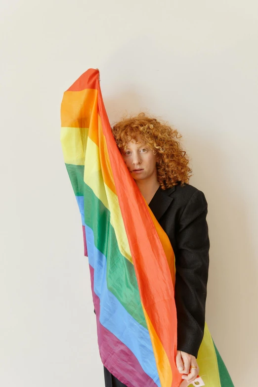a woman standing in front of a white wall holding a rainbow flag, by Harriet Zeitlin, trending on pexels, renaissance, with curly red hair, young male, holly herndon origami statue, imaan hammam