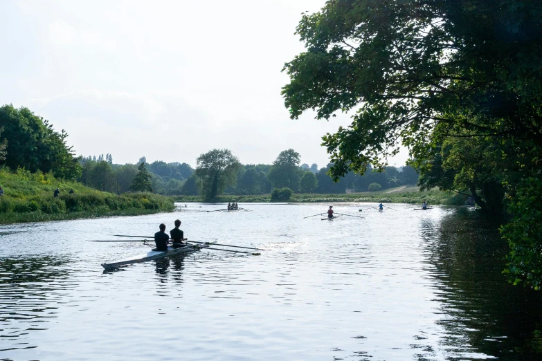 a group of people rowing down a river, by Rachel Reckitt, in the distance, college, distant photo, summer morning