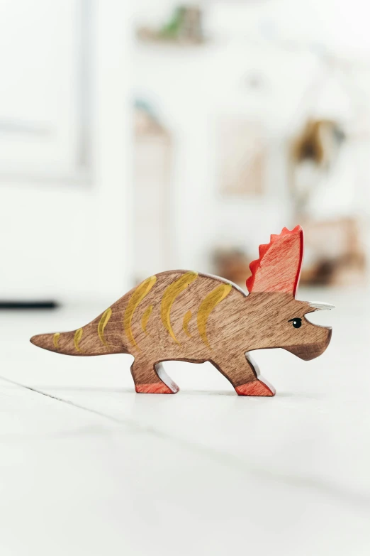 a close up of a toy dinosaur on a table, inspired by Adam Rex, holding a wood piece, multicoloured, hero shot, triceratops