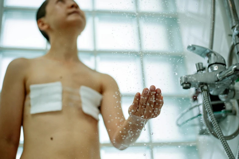 a man that is standing in front of a shower, partially cupping her hands, square, upper body image, gauze