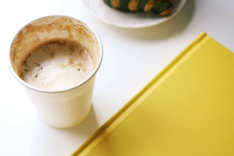 a cup of coffee and a book on a table, by Carey Morris, unsplash, minimalism, white and yellow scheme, an alien drinking horchata, 15081959 21121991 01012000 4k, high angle close up shot