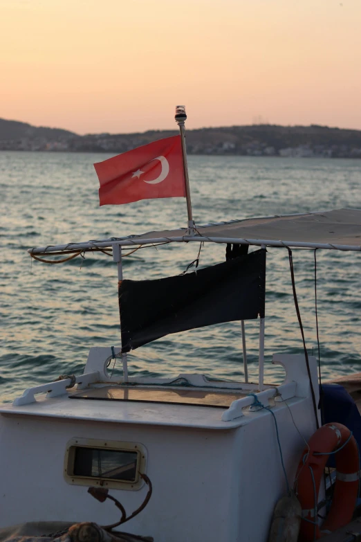 a boat sitting on top of a body of water, by Niyazi Selimoglu, hurufiyya, red flags holiday, at twilight, close - up photo