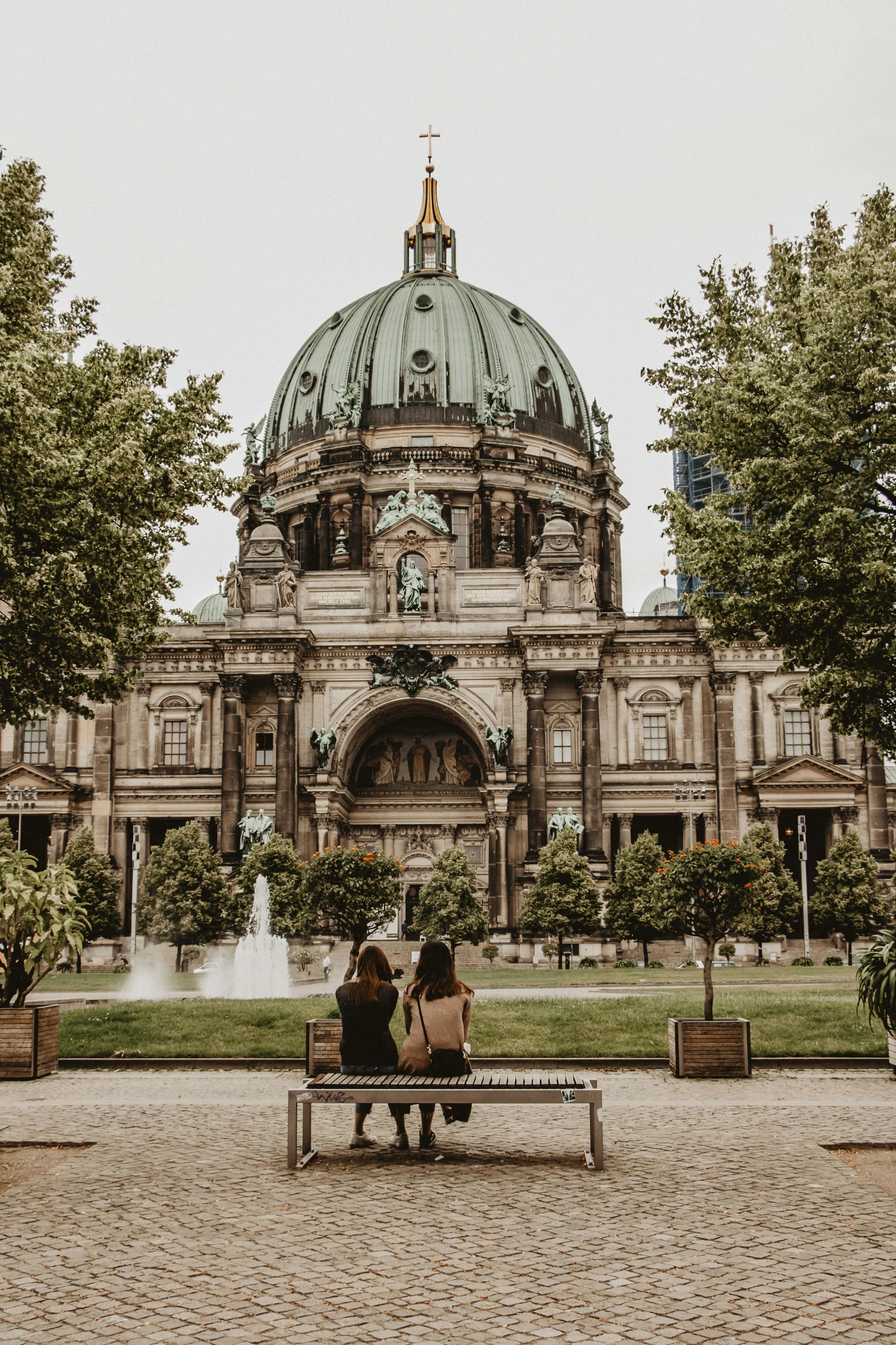 two people sitting on a bench in front of a building, by Tobias Stimmer, pexels contest winner, happening, dome, 🚿🗝📝, berlin park, beautiful setting