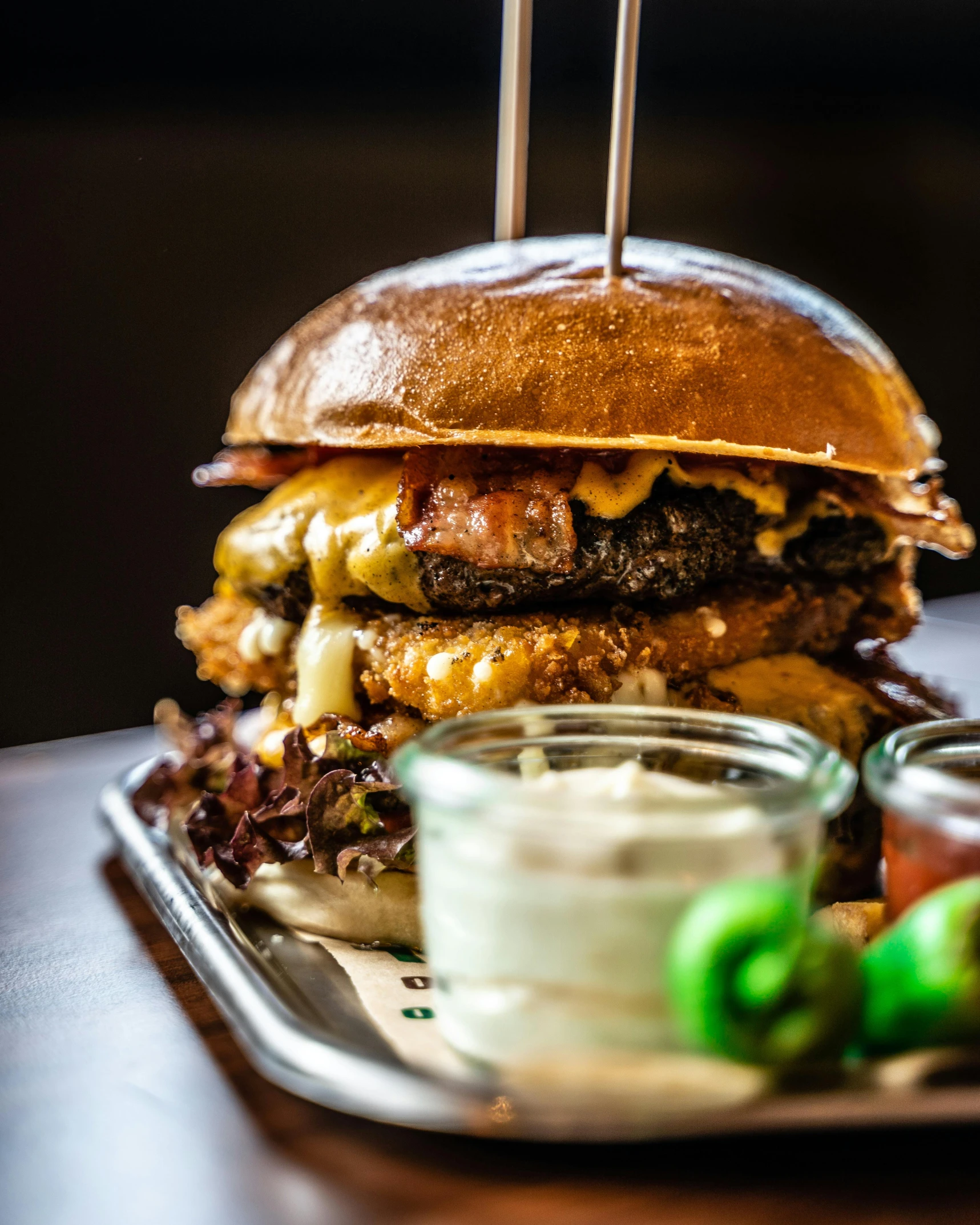 a large hamburger sitting on top of a metal tray, offering a plate of food, mesmerising, bib bang, crispy