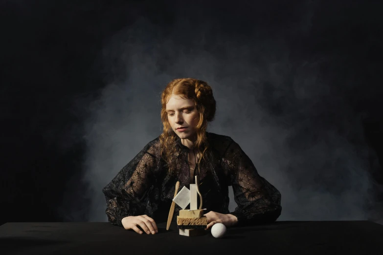 a woman sitting at a table with an object in front of her, inspired by Anna Füssli, surrealism, eleanor tomlinson, dark backdrop, portrait image, 2022 photograph