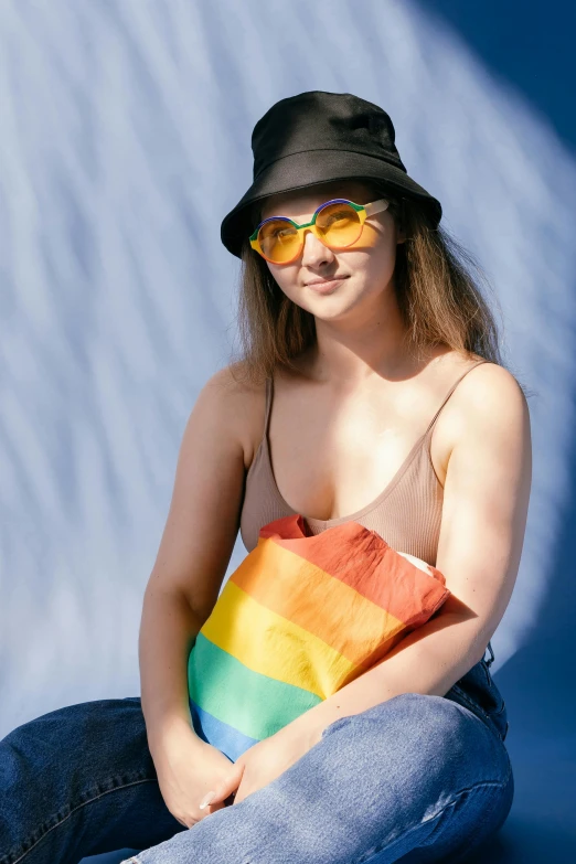 a woman sitting on a ledge wearing a hat and sunglasses, trending on pexels, color field, pride flag in background, bags, wearing a tanktop, sydney sweeney