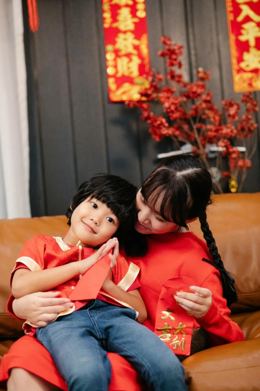 a woman sitting on top of a brown couch next to a little girl, inspired by Ni Duan, pexels contest winner, dressed in red paper bags, promotional image, boys, hugging