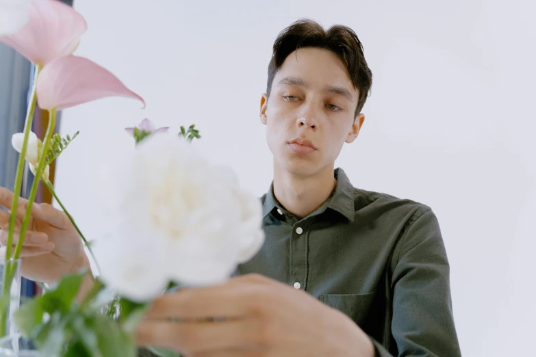 a man sitting at a table with a vase of flowers, an album cover, inspired by Fei Danxu, pexels contest winner, looking from shoulder, androgynous person, low quality footage, carrying flowers