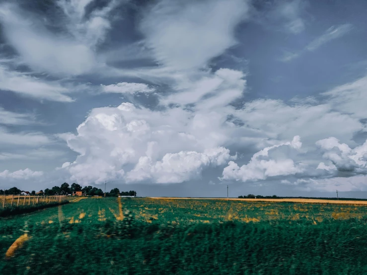 a field of tall grass under a cloudy sky, by Carey Morris, pexels contest winner, surrealism, midwest town, cumulus, slow shutter speed, patches of green fields