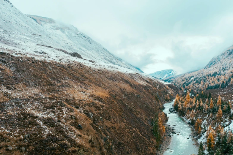 a river running through a valley in the mountains, an album cover, by Muggur, pexels contest winner, hurufiyya, dusting of snow, muted fall colors, panorama, view from the side”