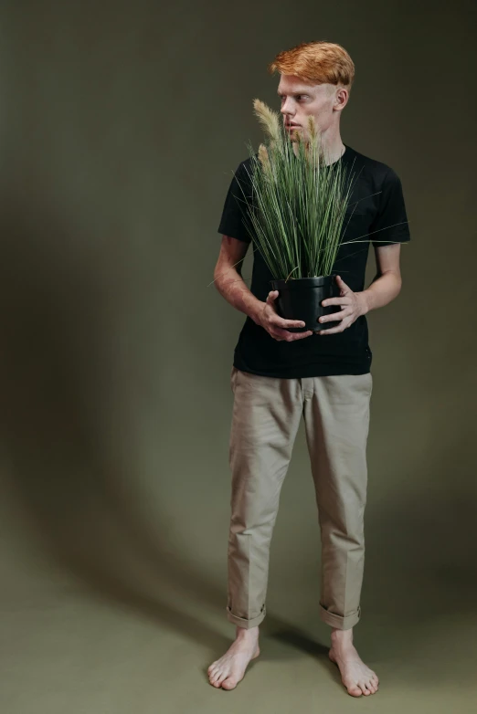 a man holding a potted plant in his hands, an album cover, unsplash, wearing pants and a t-shirt, studio portrait photo, tall grass, ( ( photograph ) )