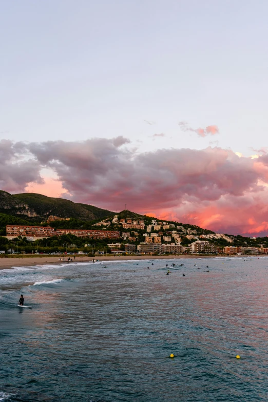 a group of people riding surfboards on top of a sandy beach, vista of a city at sunset, monaco, crimson clouds, daniel richter