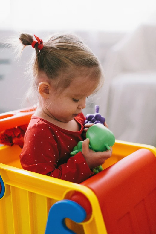 a little girl that is sitting in a toy car, brightly coloured, plastic toy, looking her shoulder, boat