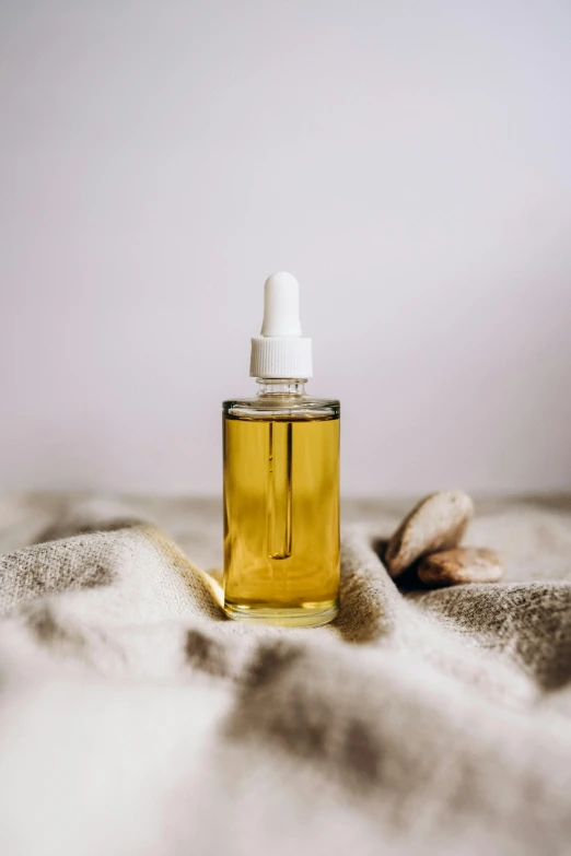 a bottle of oil sitting on top of a blanket, product image, full body image, vapor, diverse