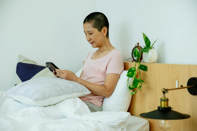 a woman sitting on a bed reading a book, inspired by Sawa Sekkyō, happening, holding a very advance phone, bald, profile image, healthcare