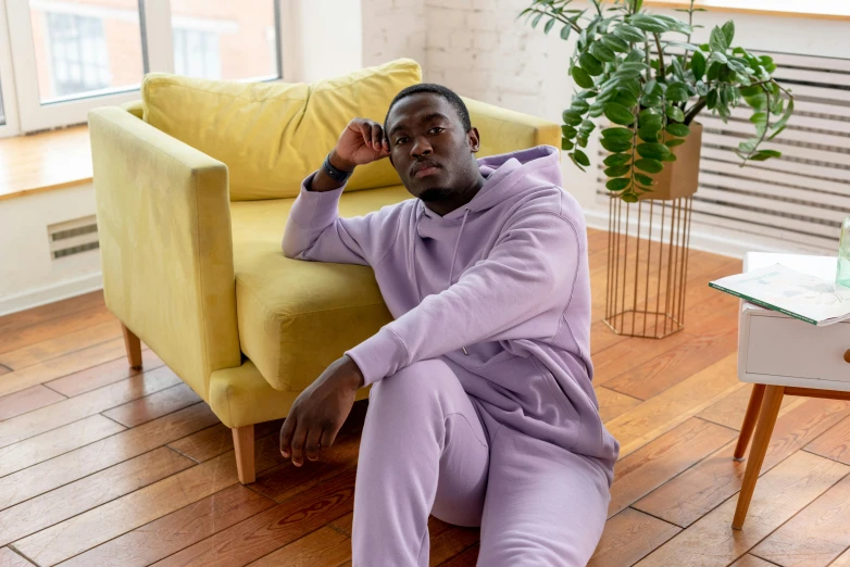 a man sitting on a couch in a living room, by Alice Mason, trending on pexels, happening, wearing a purple sweatsuit, wearing a plug suit, mkbhd, pastel clothing