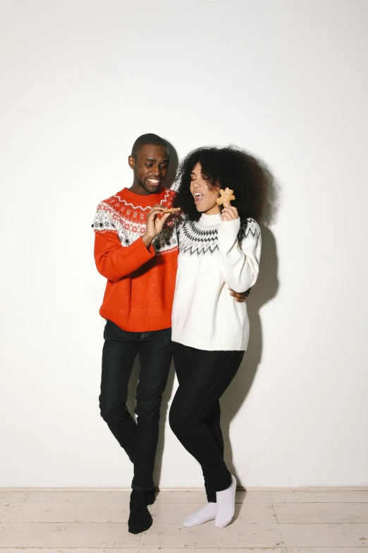 a man and a woman standing next to each other, by Lily Delissa Joseph, pexels contest winner, wearing a sweater, in front of white back drop, holiday, with afro