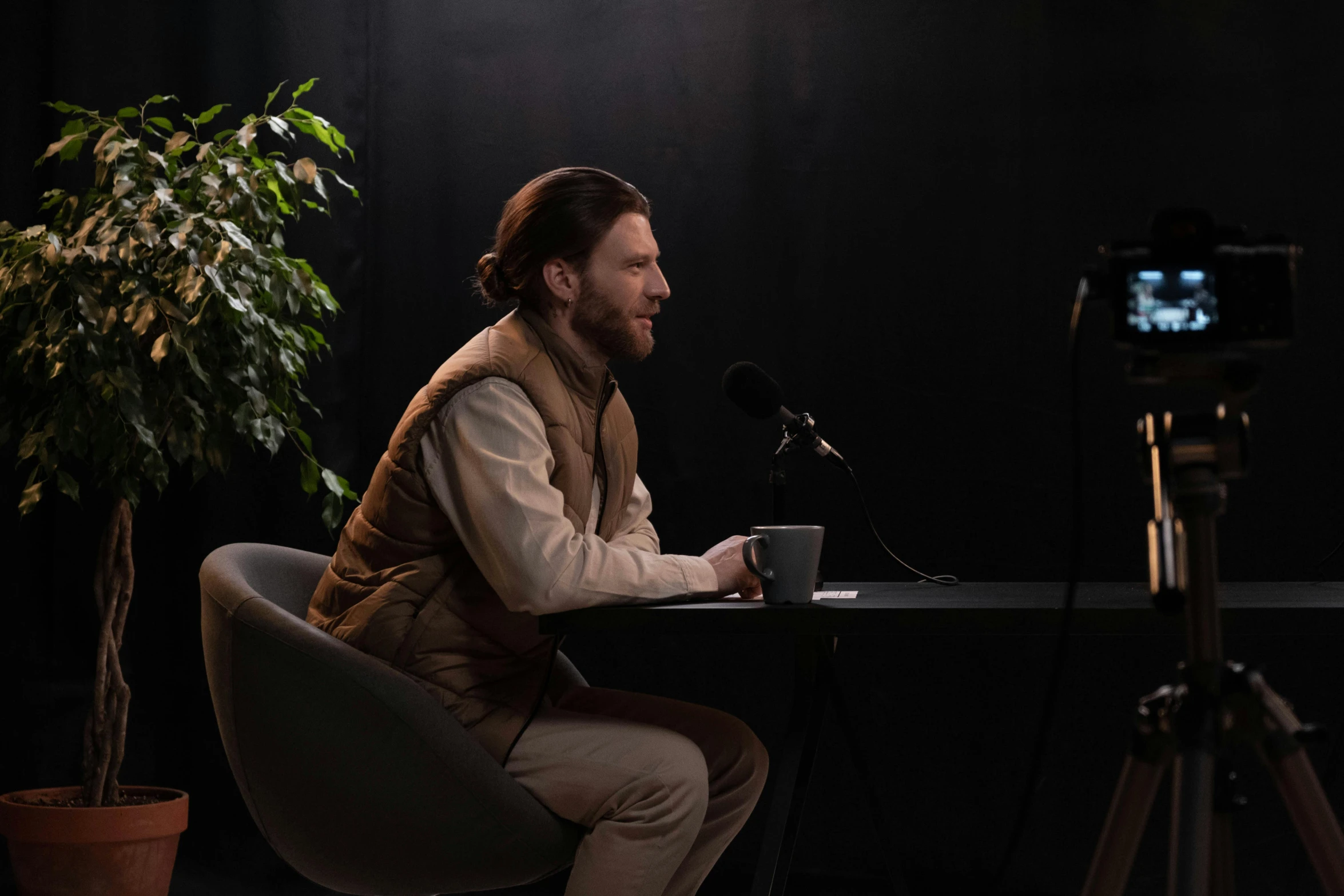 a man sitting at a table in front of a camera, set design, background image, luka mivsek, low iso