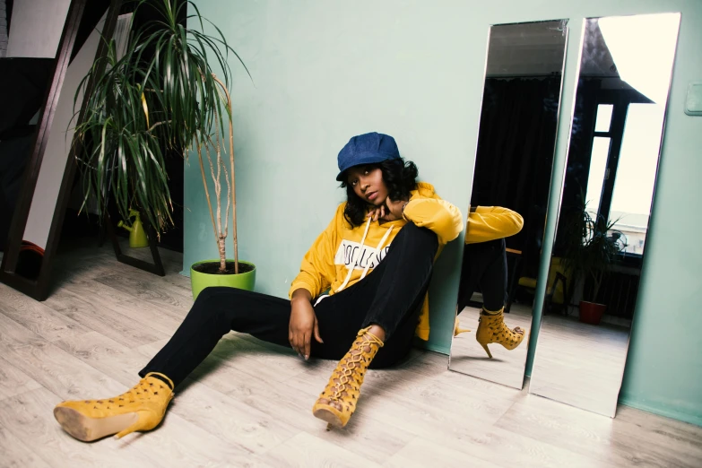 a man sitting on the floor in front of a mirror, an album cover, by Julia Pishtar, trending on pexels, yellow clothes, black young woman, yellow cap, sneaker photo