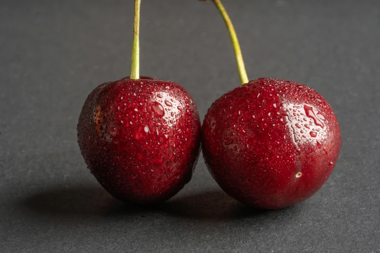 two cherries sitting next to each other on a table, an album cover, unsplash, background image, standing with a black background, high detail photo