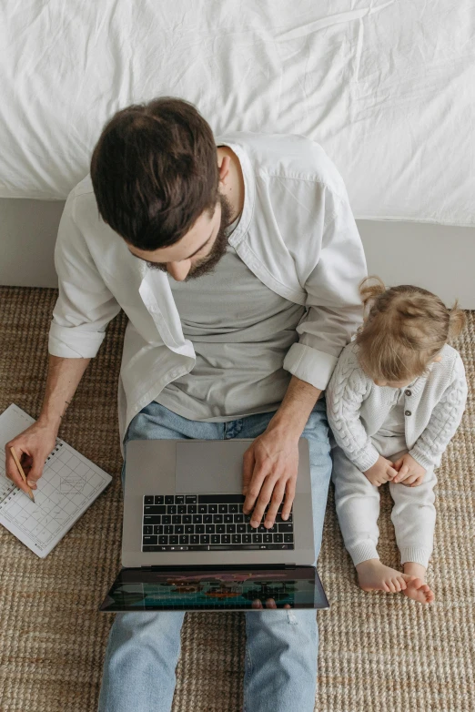 a man sitting on the floor with a laptop and a child, sitting on a bed, top - down photograph, thumbnail, trending