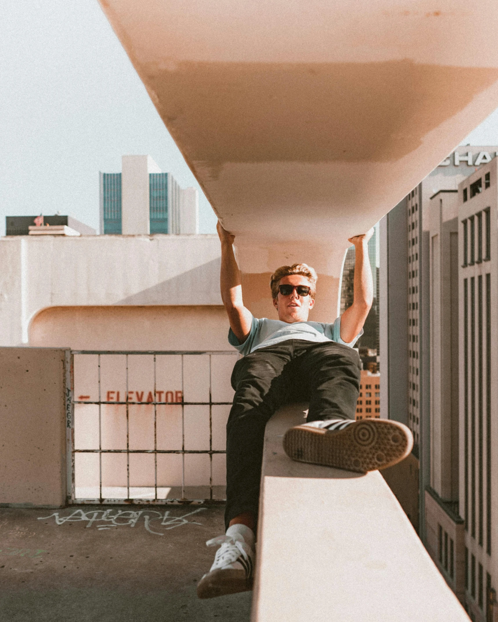 a man sitting on a ledge on top of a building, by Jessie Alexandra Dick, pexels contest winner, non-binary, wearing shades, blonde guy, plain walls |light hearted