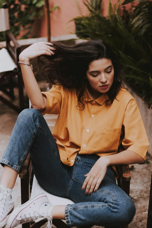 a woman sitting on a chair with her hair blowing in the wind, trending on pexels, collared shirt, ochre, jeans and t shirt, curated collection