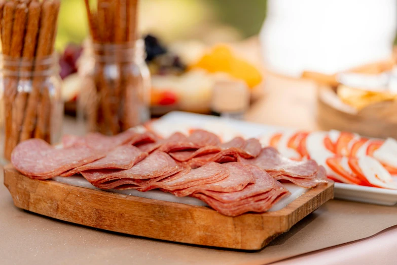 a wooden cutting board sitting on top of a table, salami, profile image, offering a plate of food, during the day