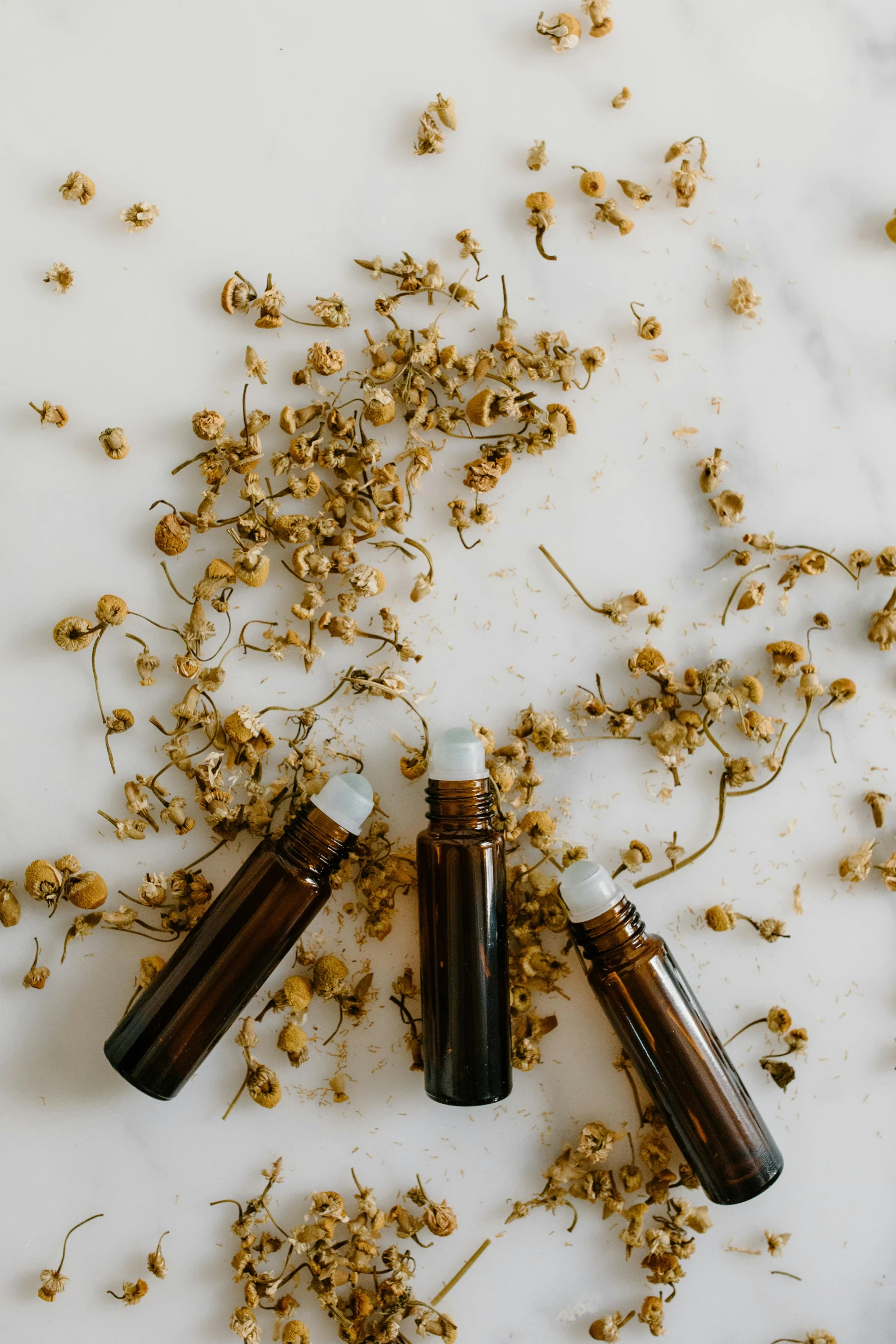 three bottles of essential oils on a marble surface, by Jessie Algie, chamomile, thumbnail, brown, indoor shot