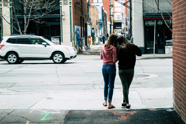 a couple of women standing next to each other on a sidewalk, trending on unsplash, happening, north melbourne street, seen from the back, teenage, lesbian embrace