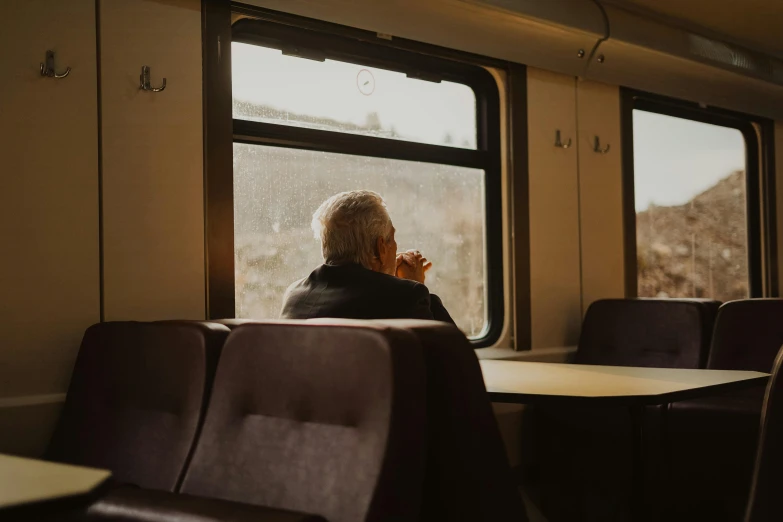 a person sitting in a train looking out a window, by Kristian Zahrtmann, pexels contest winner, sitting on a mocha-colored table, an oldman, youtube thumbnail, lonely