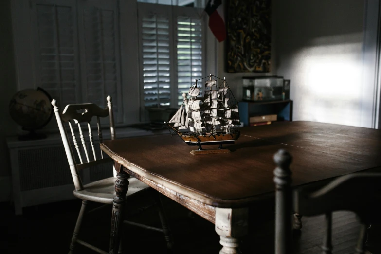 a model ship sitting on top of a wooden table, unsplash contest winner, photorealism, interior of a victorian house, 1792, medium format. soft light, dining table