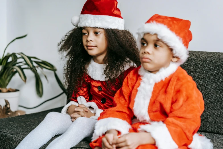 a couple of kids sitting on top of a couch, by Emma Andijewska, pexels, santa clause, with brown skin, profile image, wearing festive clothing