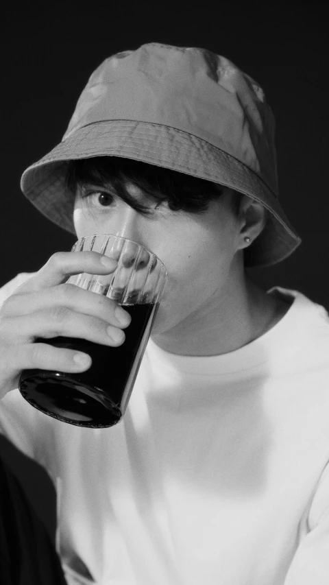 a black and white photo of a man drinking a beer, a black and white photo, inspired by Huang Gongwang, pexels, photorealism, 1 7 - year - old boy thin face, baggy clothing and hat, juice, male ulzzang