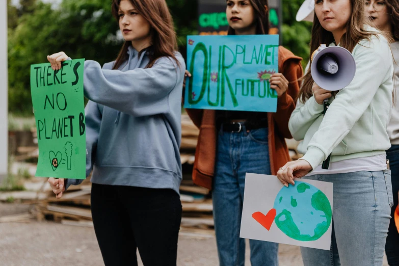 a group of people standing next to each other holding signs, by Julia Pishtar, trending on pexels, mother earth, college girls, background image, green tonalities