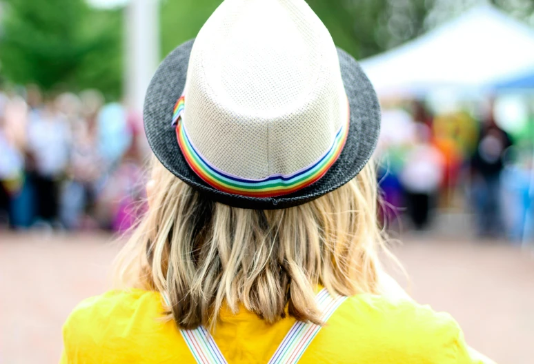 a close up of a person wearing a hat, pride parade, beautiful surroundings, yellow hair, back of head