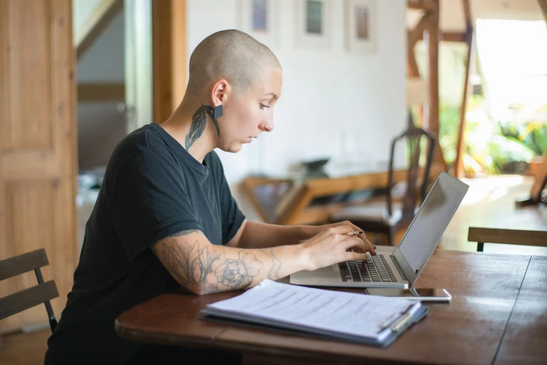 a person sitting at a table with a laptop, by Meredith Dillman, pexels, renaissance, brown buzzcut, tattooed, home office, covered in