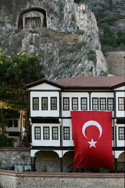a building with a flag in front of a mountain, inspired by Yasar Vurdem, hurufiyya, slide show, turkey, tudor, cliffside town