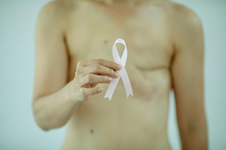 a close up of a person holding a pink ribbon, bare chest, lean man with light tan skin, 2022 photograph, injured