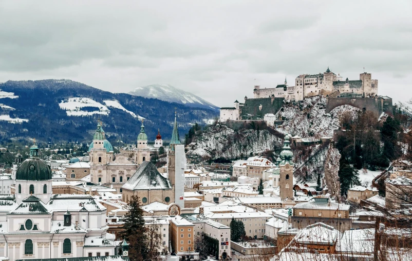 a view of a city with mountains in the background, a photo, pexels contest winner, baroque, covered in snow, travel guide, white, austria