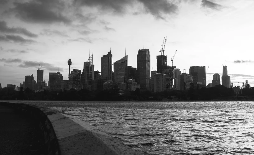 a black and white photo of a city skyline, a black and white photo, inspired by Sydney Carline, pexels, hurufiyya, overcast dusk, the photo was taken from a boat, taken at golden hour, pose 4 of 1 6