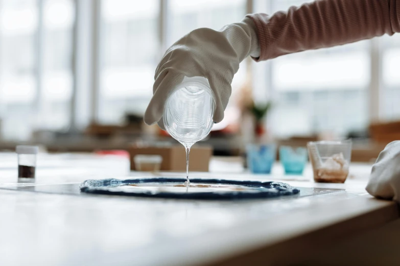 a person pouring something into a bowl on a table, inspired by Vija Celmins, trending on unsplash, process art, scientific glassware, lightblue acrylic paintdrip tar, silicone skin, in a workshop