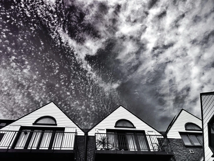 a black and white photo of a row of houses, unsplash, precisionism, with overhead cloudy!!!!! skies, view from ground level, eyelevel!!! view!!! photography, spiral clouds