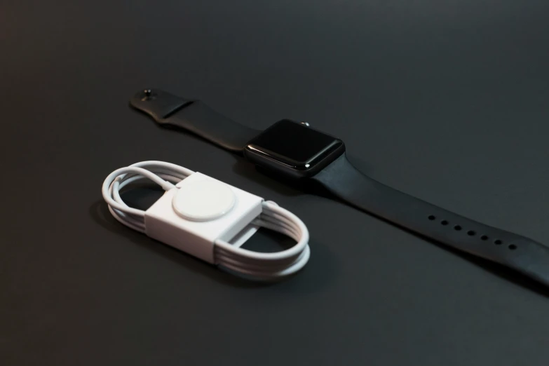 an apple watch sitting on top of a table next to a charger, a black and white photo, minimalism, on a flat color black background, bandoliers, thick wires, sleek white