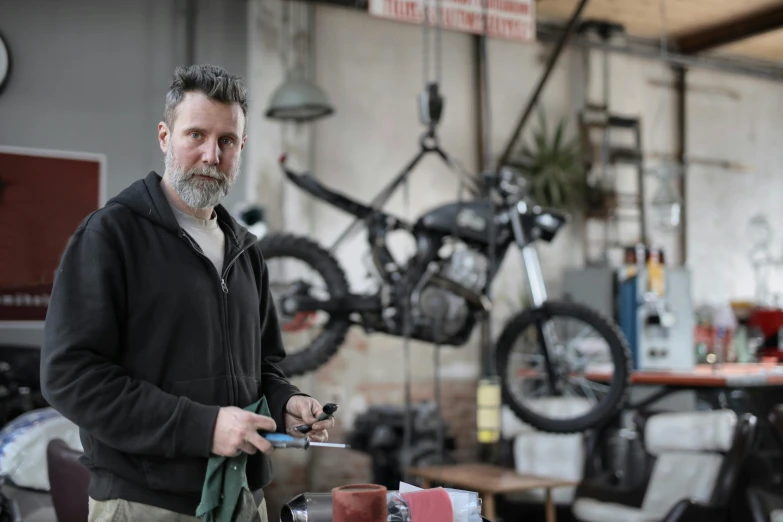 a man standing next to a motorcycle in a garage, pexels contest winner, blacksmith product design, scrap metal on workbenches, avatar image, mechanised