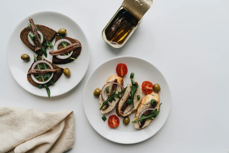 two plates of food on a white table, unsplash, modernism, sardine in a can, olive oil, cuttlefish, high quality product image”