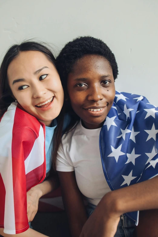 a woman sitting next to a boy holding an american flag, a portrait, trending on unsplash, chinese woman, lesbian embrace, with brown skin, high school girls