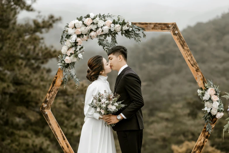 a bride and groom kissing in front of a wedding arch, pexels contest winner, quy ho, manuka, picture frames, nebulous bouquets