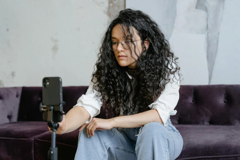 a woman sitting on top of a purple couch, a polaroid photo, trending on pexels, serial art, long black curly hair, phone recording, with curls, wearing a dark shirt and jeans