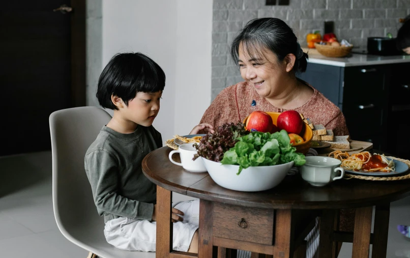 a woman and a child sitting at a table with food, pexels contest winner, fruit bowl, avatar image, asian male, high quality image
